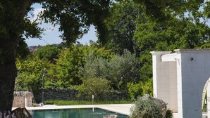 A swimming pool surrounded by stone walls and greenery, with a clear view of the sky and trees in the background. - Trullo Cinquenoci Jr Suite (Locorotondo)