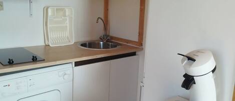 A compact kitchen with a microwave, sink, washing machine, and coffee maker.