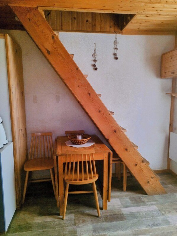A wooden staircase leading to an upper level, a small wooden table with chairs, and a wall-mounted light fixture.
