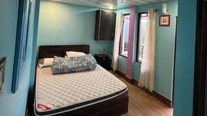 A bedroom with a bed, a nightstand, a wall-mounted TV, and a window with curtains. - Manjushree Homestay (Darjeeling)