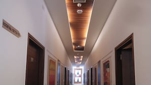 Un couloir d’hôtel avec un tapis à motifs en zigzag, des panneaux de plafond en bois et des portes portant l’indication du numéro de chambre.