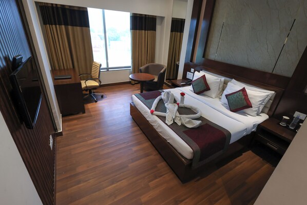A hotel room with a large bed, a desk, a chair, and a TV.