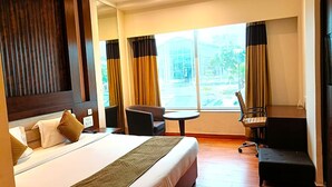 Une chambre d’hôtel avec un lit, un bureau, une chaise et une grande fenêtre avec des rideaux.