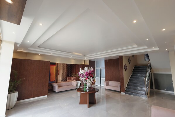 A spacious living area with a staircase, a round coffee table with a floral arrangement, and a large potted plant. - Tivoli Royal Palace (Palwal)