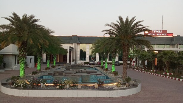 Un espace aménagé avec des palmiers, une fontaine et un bâtiment portant l’inscription « TIVOLI ROYAL PALACE MILLENNIUM HOUSE ».