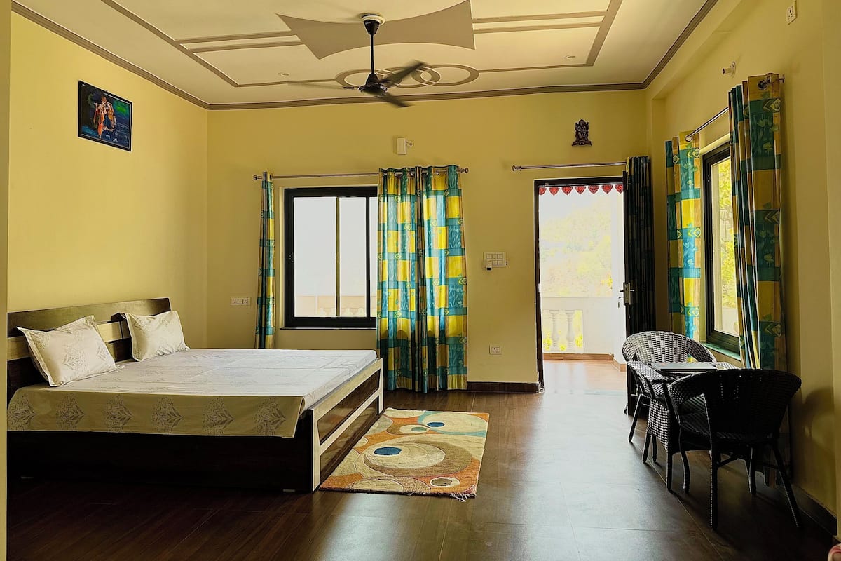 Un dormitorio con cama, ventilador de techo, ventana con cortinas y vistas al exterior.