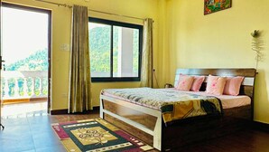 A bedroom with a bed, a ceiling fan, a window with curtains, a door, and a view of greenery outside. - Kailasham Homestay (Kyarki)