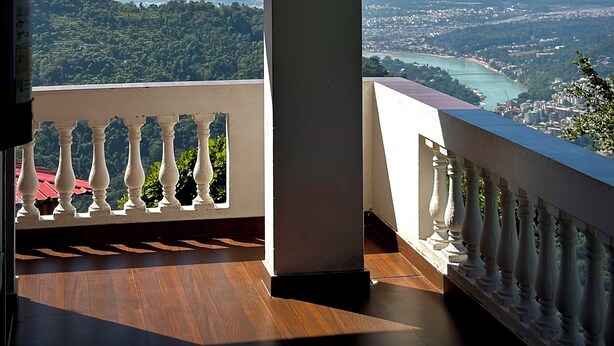 A balcony with a view of a coastal city and mountains. - Kailasham Homestay (Kyarki)