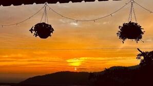 A sunset with hanging plants and a view of a hilly landscape. - Kailasham Homestay (Kyarki)