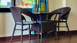 A room with a window, two wicker chairs, a small table, and a curtain with a geometric pattern. - Kailasham Homestay (Kyarki)