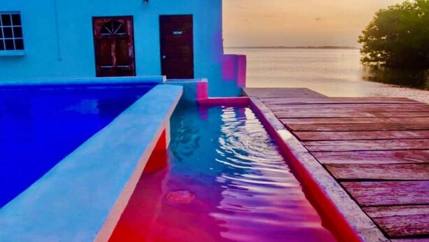 A swimming pool with a wooden deck and a building in the background. - Poolside Seaview Studio With Infinity Pool & Overwater Deck Near Airport, 1st FL (Belize City)