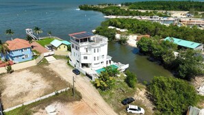A large, multi-story building with a rooftop solar panel, surrounded by a body of water and greenery. - Poolside Seaview Studio With Infinity Pool & Overwater Deck Near Airport, 1st FL (Belize City)