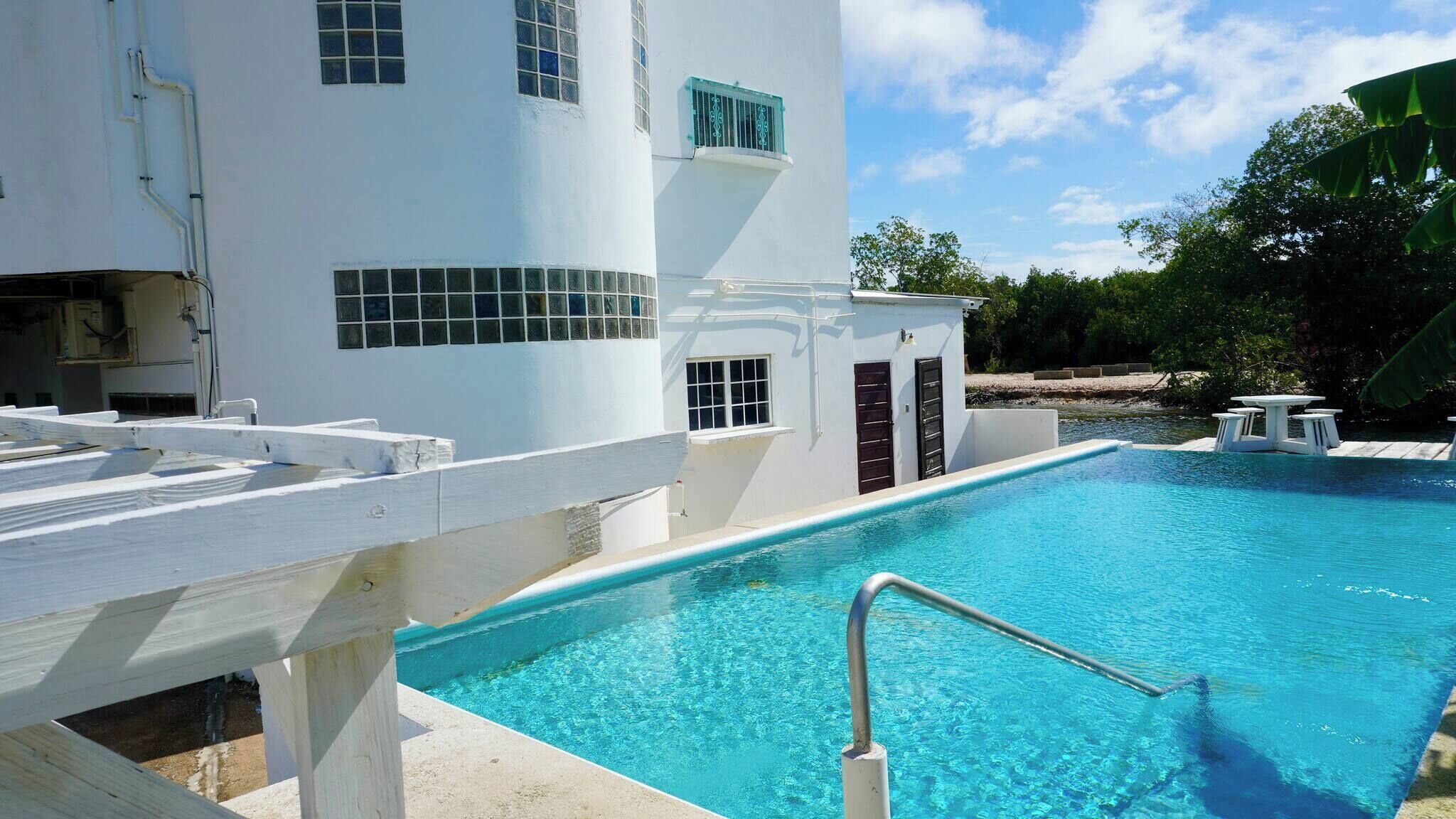 A pool area with a white building, a diving board, and a small table with chairs.