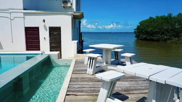 Un área de piscina con una terraza de madera, sillas de descanso blancas y vista al mar.