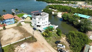 A coastal property with a large white building featuring a rooftop pool, surrounded by lush greenery and a clear view of the ocean. - See Belize Seabreeze Sea View Studio With Balcony, Pool & Overwater Deck, 2nd FL (Belize City)
