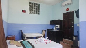 A small room with a bed, a table, a microwave, and a cabinet. There is a window with a grid pattern and a sign that says "NO SMOKING". - See Belize Seabreeze Sea View Studio With Balcony, Pool & Overwater Deck, 2nd FL (Belize City)