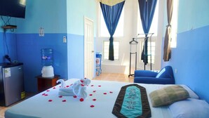 A hotel room with a bed, a water dispenser, a desk, a TV, and a window with curtains. - See Belize Seabreeze Sea View Studio With Balcony, Pool & Overwater Deck, 2nd FL (Belize City)
