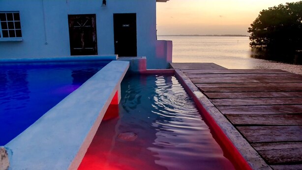 A swimming pool with a wooden deck and a view of the sea at sunset. - See Belize Seabreeze Sea View Studio With Balcony, Pool & Overwater Deck, 2nd FL (Belize City)