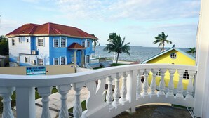 A coastal property with a blue building and a yellow structure, featuring a white balcony railing. - See Belize Seabreeze Sea View Studio With Balcony, Pool & Overwater Deck, 2nd FL (Belize City)