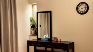 Una habitación con un escritorio negro, un espejo, un reloj, una planta y una cortina.