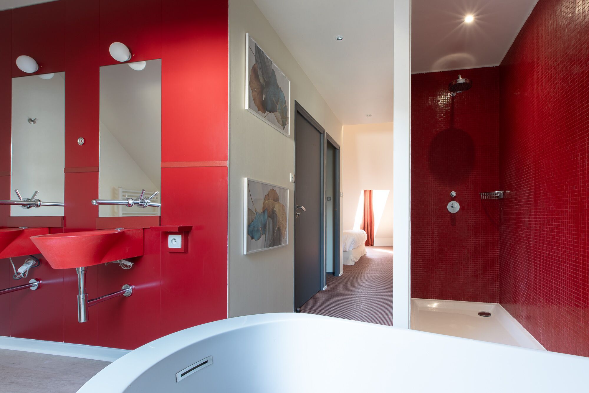 Un baño moderno con una decoración en rojo y blanco, que incluye una bañera grande, dos lavamanos y una zona de ducha.