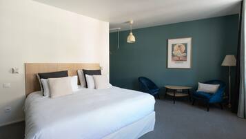 Une chambre d’hôtel avec un grand lit, deux chaises, une petite table et un tableau au mur.