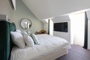 Ein modernes Hotelzimmer mit einem großen Bett, einem runden Spiegel, einem Fernseher und einem Fenster mit Vorhängen.
