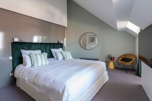Ein modernes Hotelzimmer mit einem großen Bett, einem runden Spiegel, einem kleinen Tisch mit Lampe und einem Sessel.