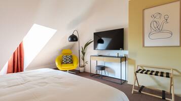 A modern hotel room with a large bed, a desk with a flat-screen TV, a yellow armchair, and a painting on the wall.