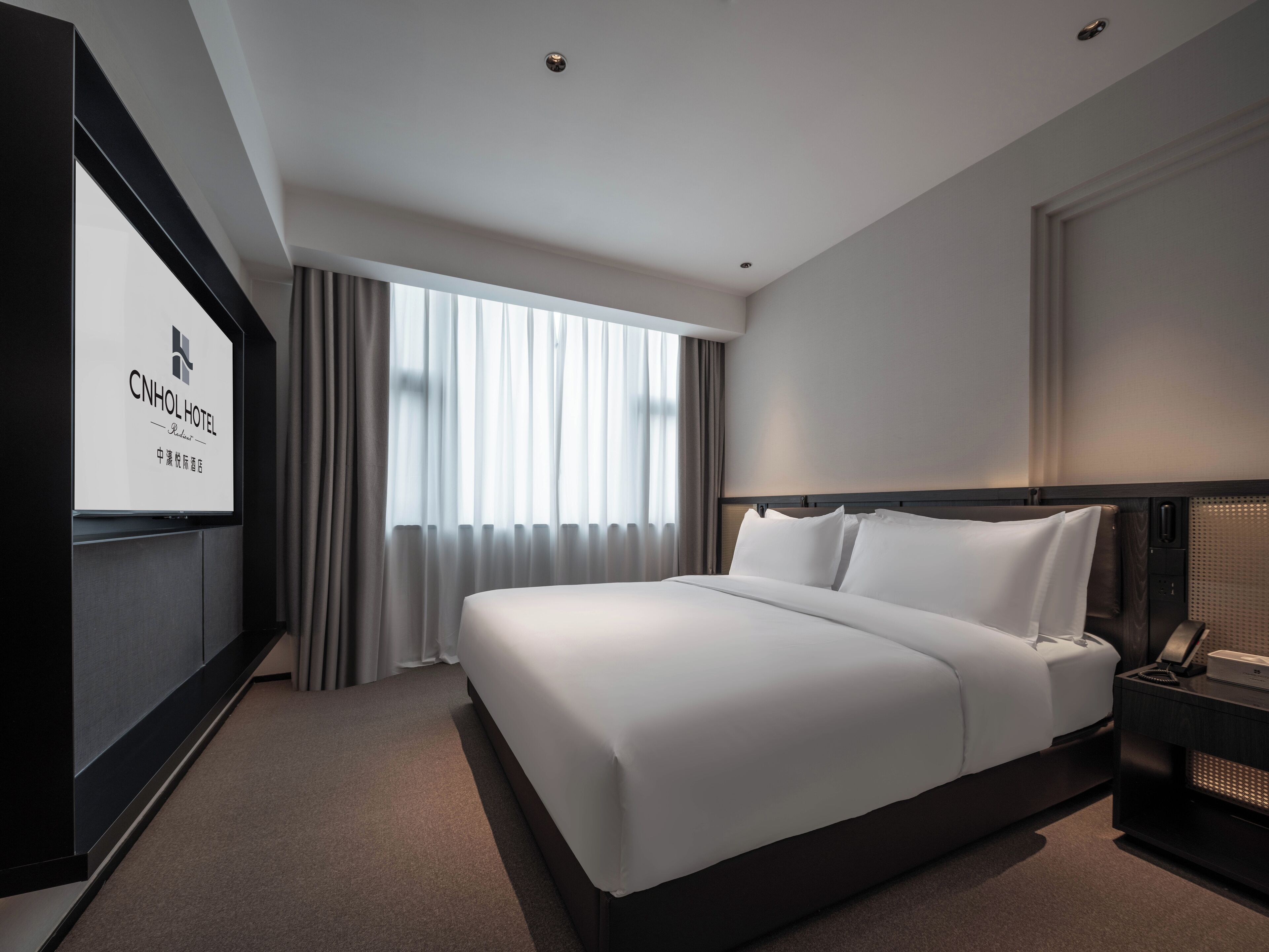 A modern hotel room with a large bed, a TV, and a window with curtains.