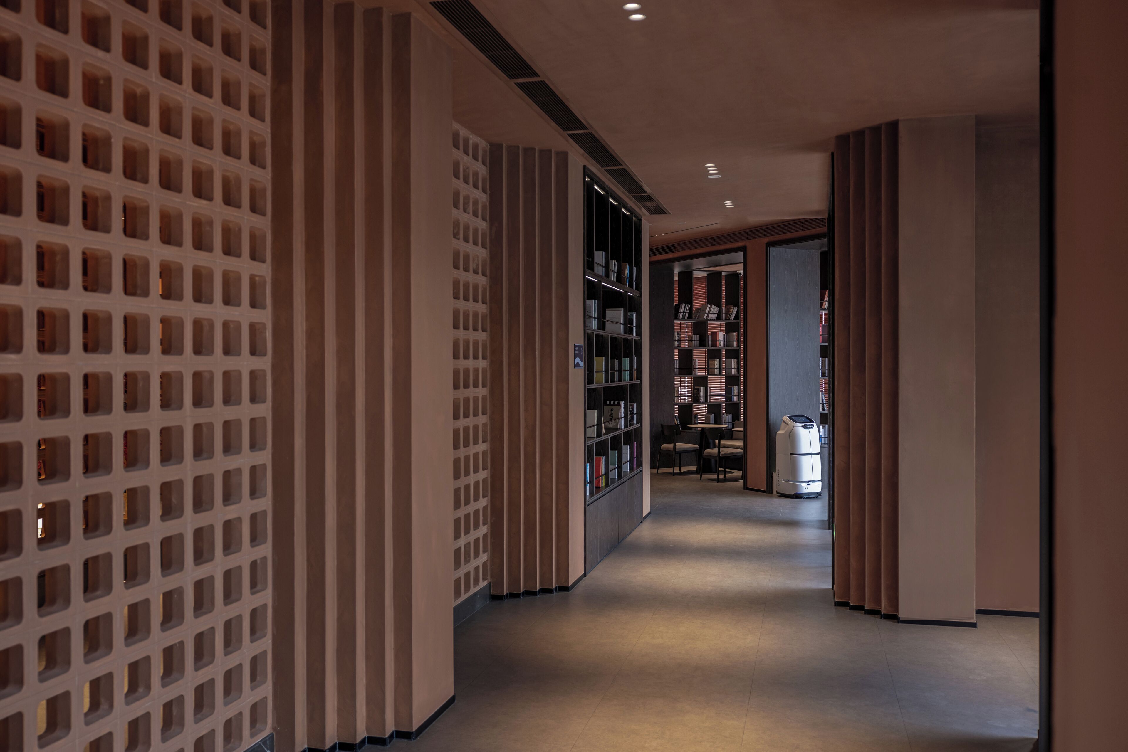 A hallway with a modern design, featuring a patterned wall, a bookshelf, and a trash bin.