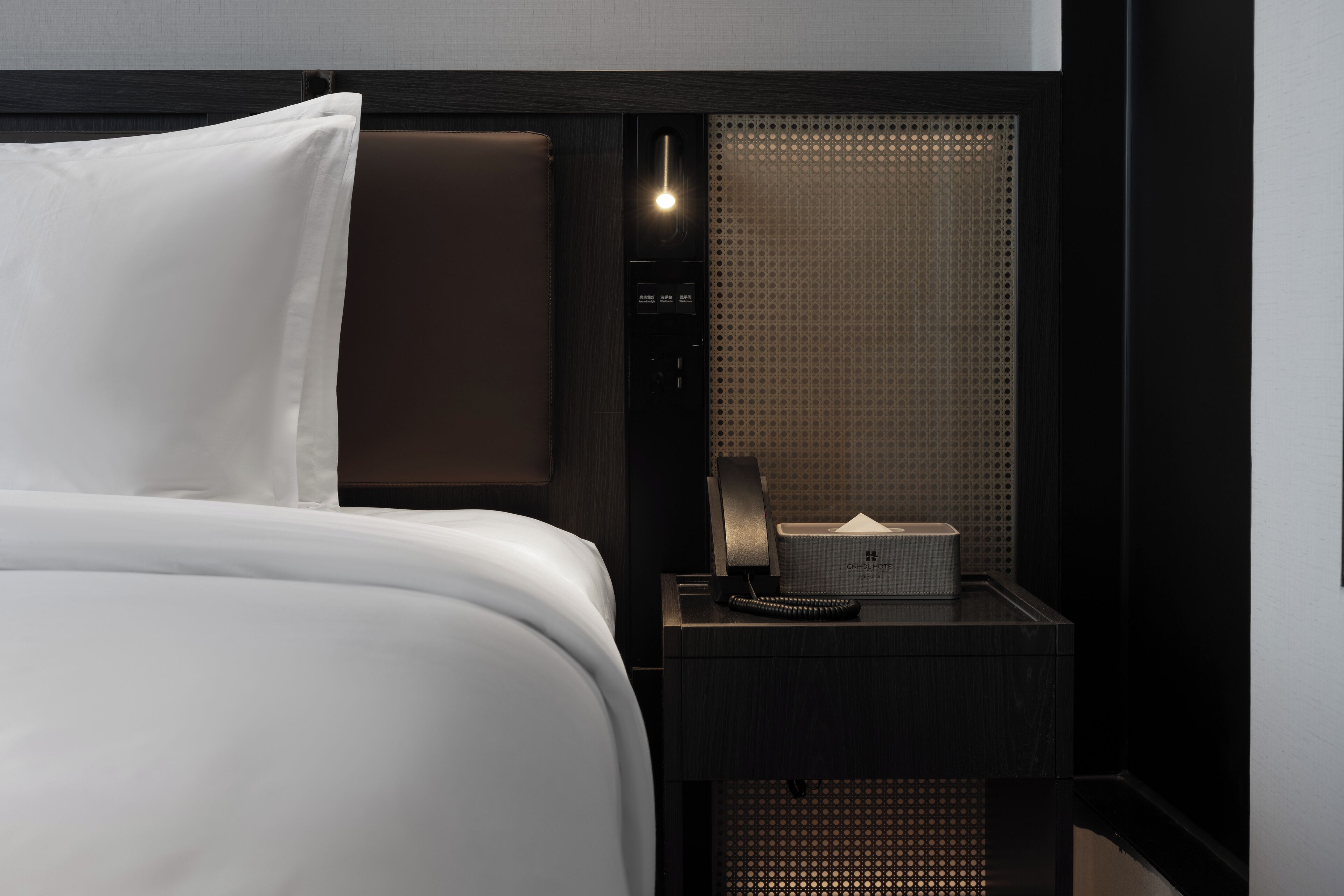 Une chambre d’hôtel avec un lit bien fait, une table de chevet avec une lampe, une télécommande et un mini-bar.