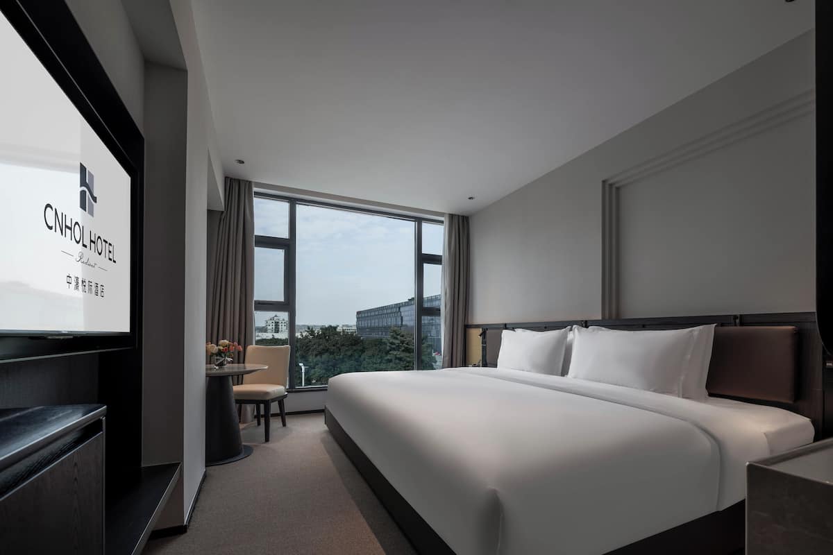 A modern hotel room with a large bed, a desk, and a TV.