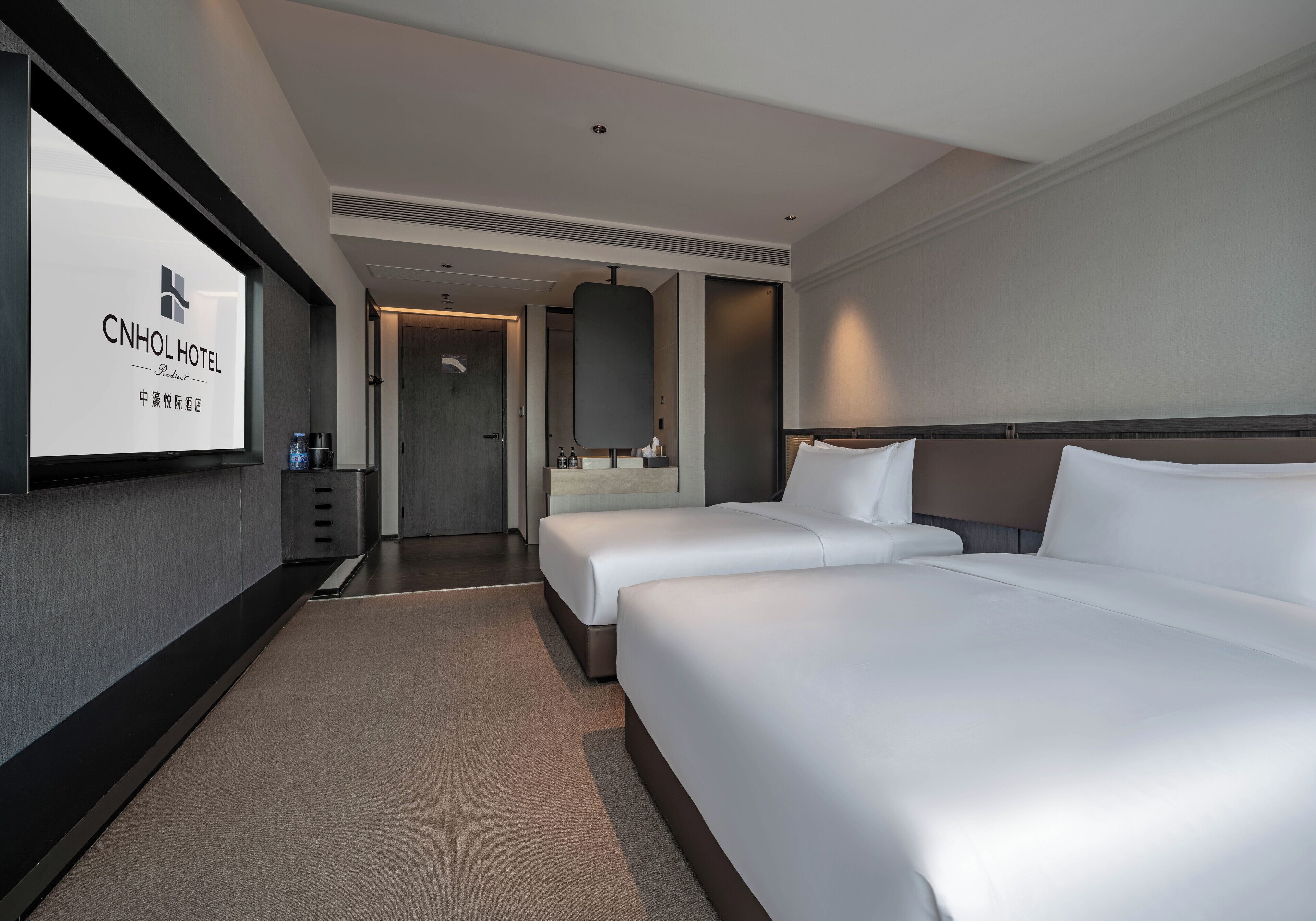 Ein Hotelzimmer mit zwei Betten, einem großen Spiegel, einer Minibar und einem Fernseher, der den Namen des Hotels zeigt.