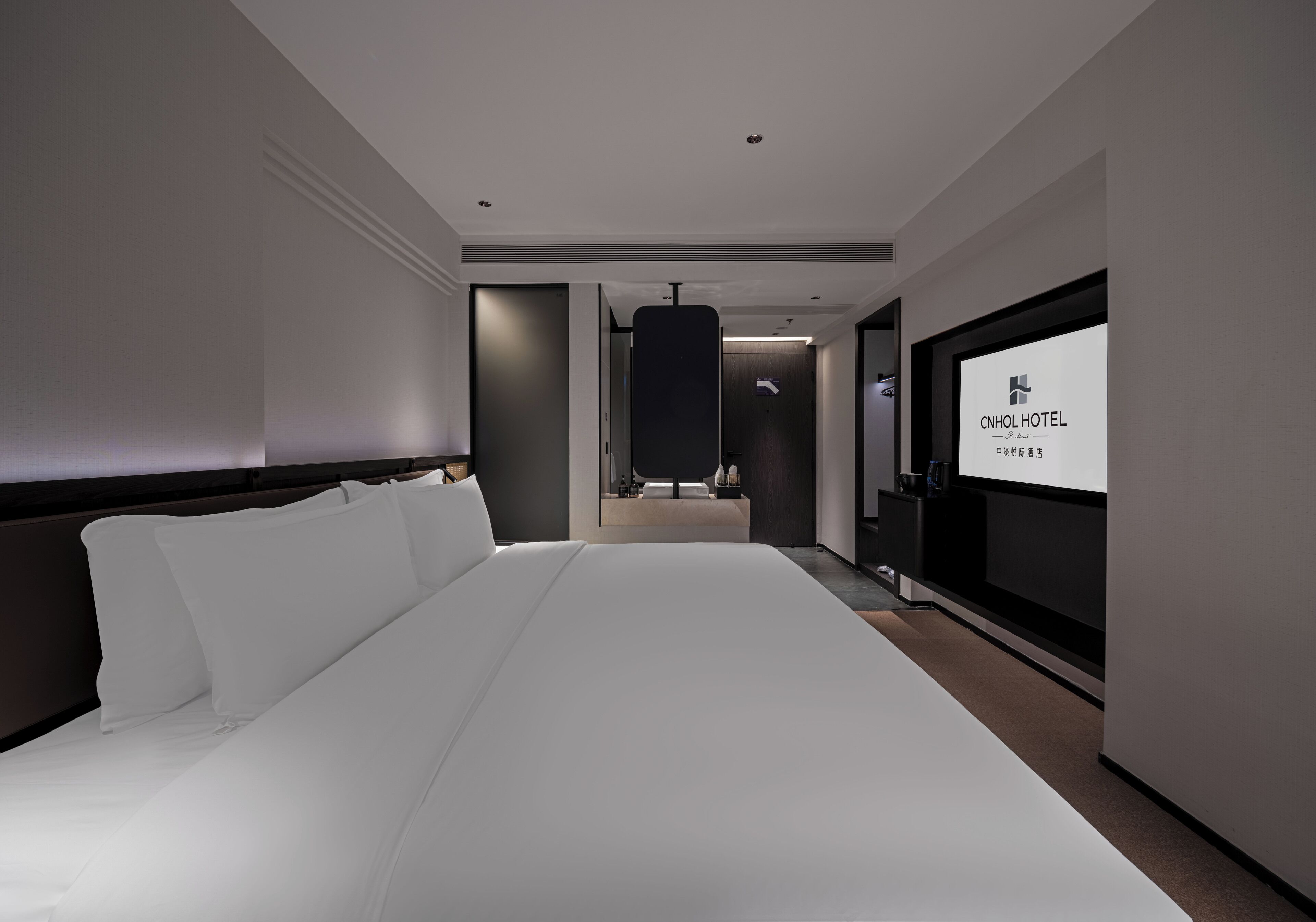 A modern hotel room with a large bed, a TV, and a desk.
