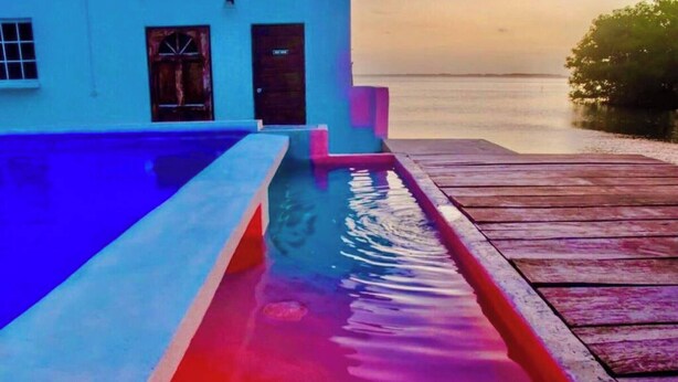 A pool with a wooden deck and a building in the background. - See Belize Tranquil Sea View Studio With (Belize City)