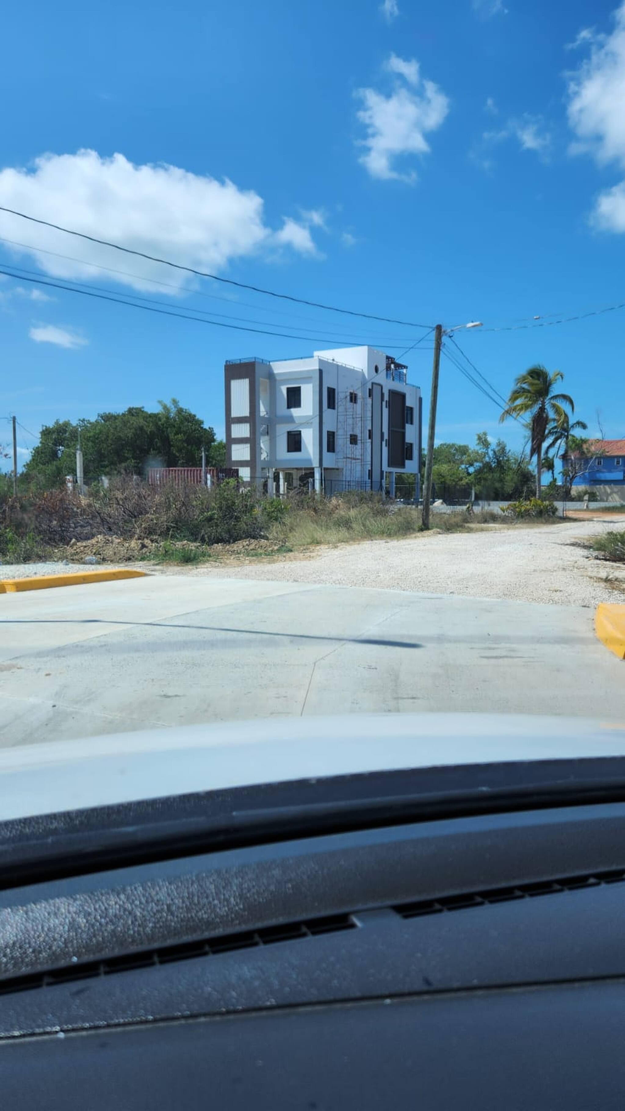 Un edificio moderno con fachada blanca y varias ventanas, situado cerca de una calle con bordillo amarillo.