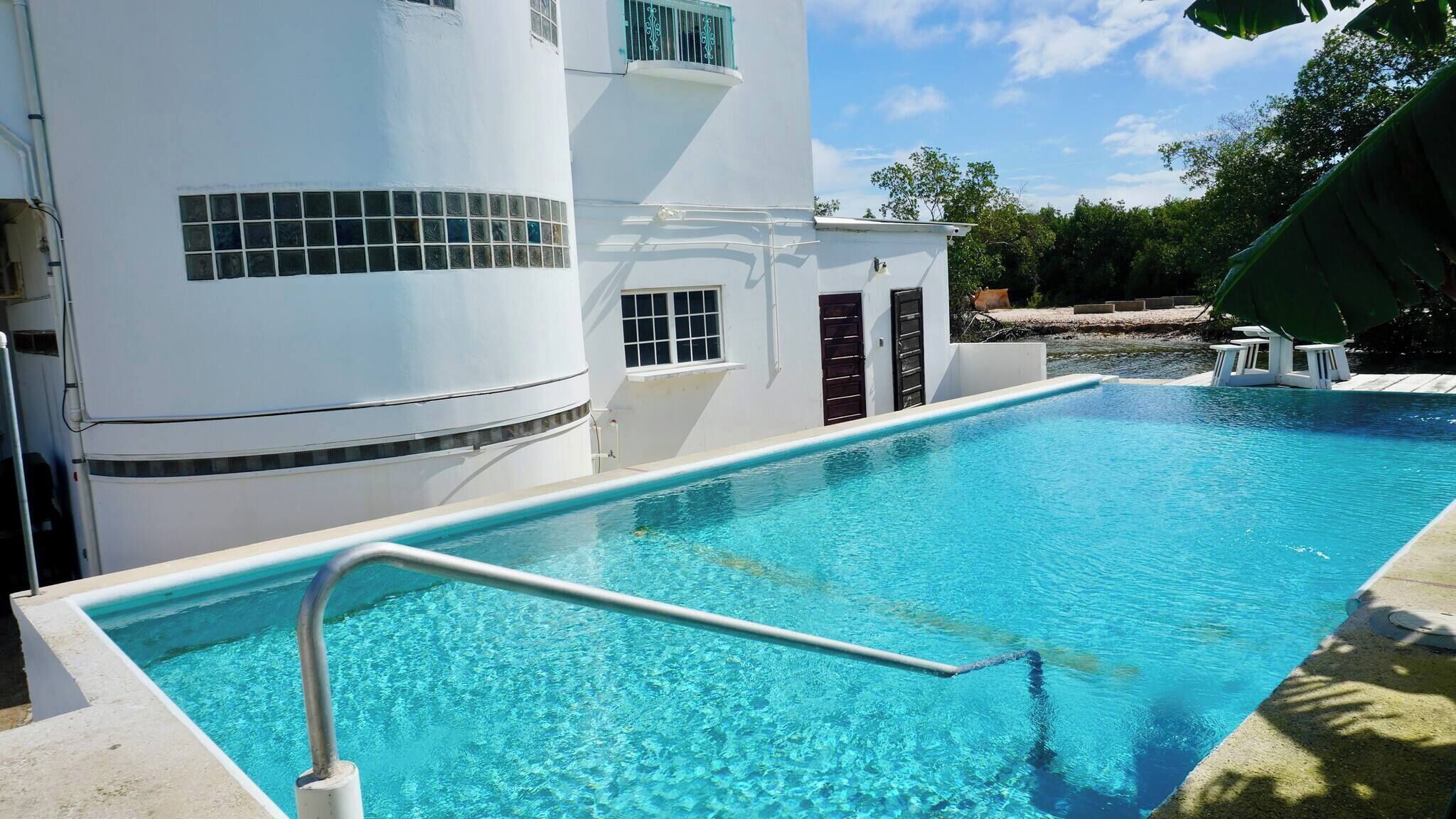 A swimming pool with a clear blue water, surrounded by a white building with a curved facade and windows.