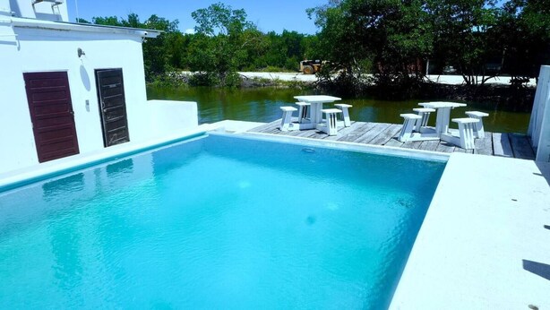A rectangular swimming pool with a wooden deck and white lounge chairs. - Sea Belize Relaxing Studio w Sea View Pool & Overwater Deck Near Airport, 1st FL (Belize City)