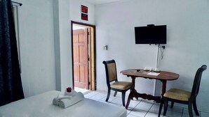 A hotel room with a bed, a table with chairs, a TV mounted on the wall, and an exit sign above the door. - Sea Belize Relaxing Studio w Sea View Pool & Overwater Deck Near Airport, 1st FL (Belize City)