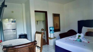 A hotel room with a bed, a desk, a chair, a refrigerator, a water dispenser, and a mirror.