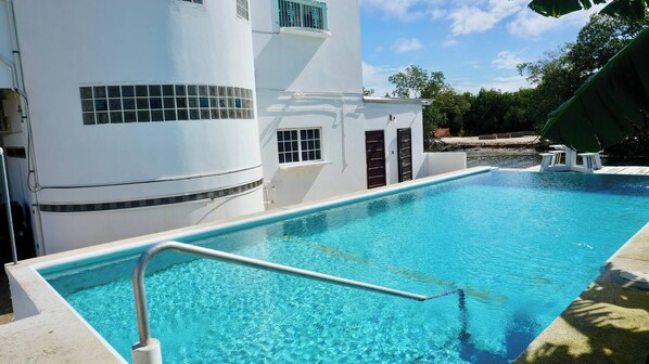 A swimming pool with a clear blue water, surrounded by a white building with a curved facade and windows.