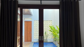 A room with a bed, a sliding glass door leading to a pool area, and a wooden door in the background. - Nusa Dua 3BR Villa • Perfect for Families (Bali)