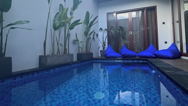 A modern pool area with tiled flooring, potted plants, and blue cushions. - Nusa Dua 3BR Villa • Perfect for Families (Bali)