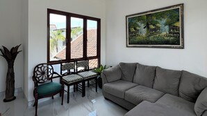 A modern living room with a marble floor, a grey sofa, a dining table with chairs, a large window, and a ceiling light fixture. - Nusa Dua 3BR Villa • Perfect for Families (Bali)