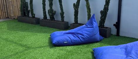 A rooftop garden with artificial grass, blue cushions, and cacti against a white wall.