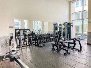 Uma academia com diversos equipamentos de exercícios, incluindo halteres, um aparelho de supino e uma esteira.