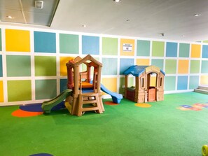 Zona de juegos infantiles con un tobogán, una estructura para escalar y una casita.