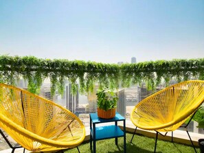A balcony with two yellow chairs, a small table, and a potted plant.
