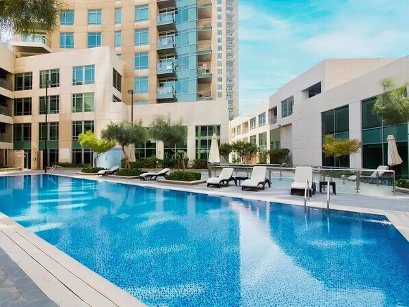 A modern hotel with a swimming pool, lounge chairs, and a high-rise building in the background.